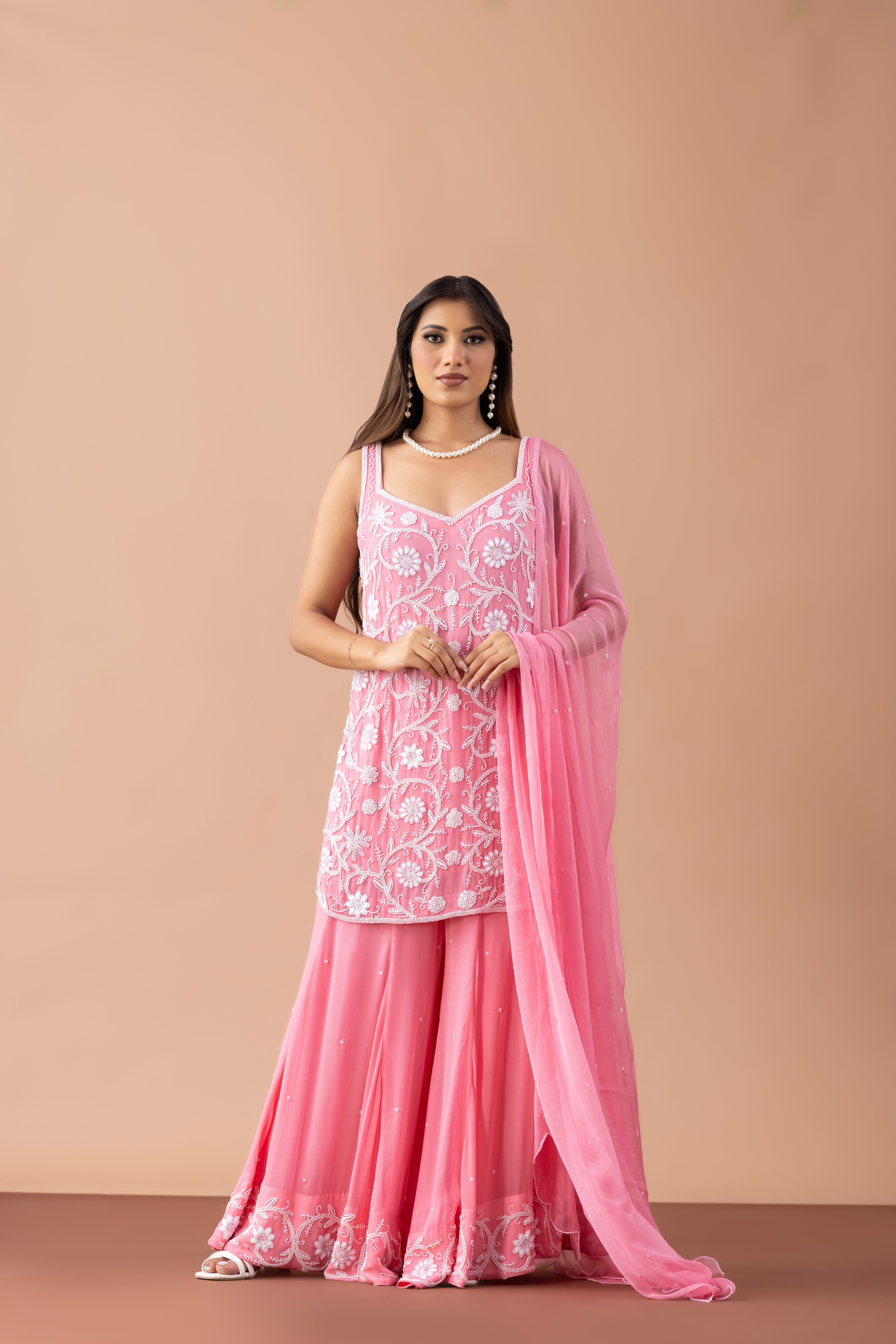 Woman wearing a pink traditional outfit with a matching dupatta against a beige background