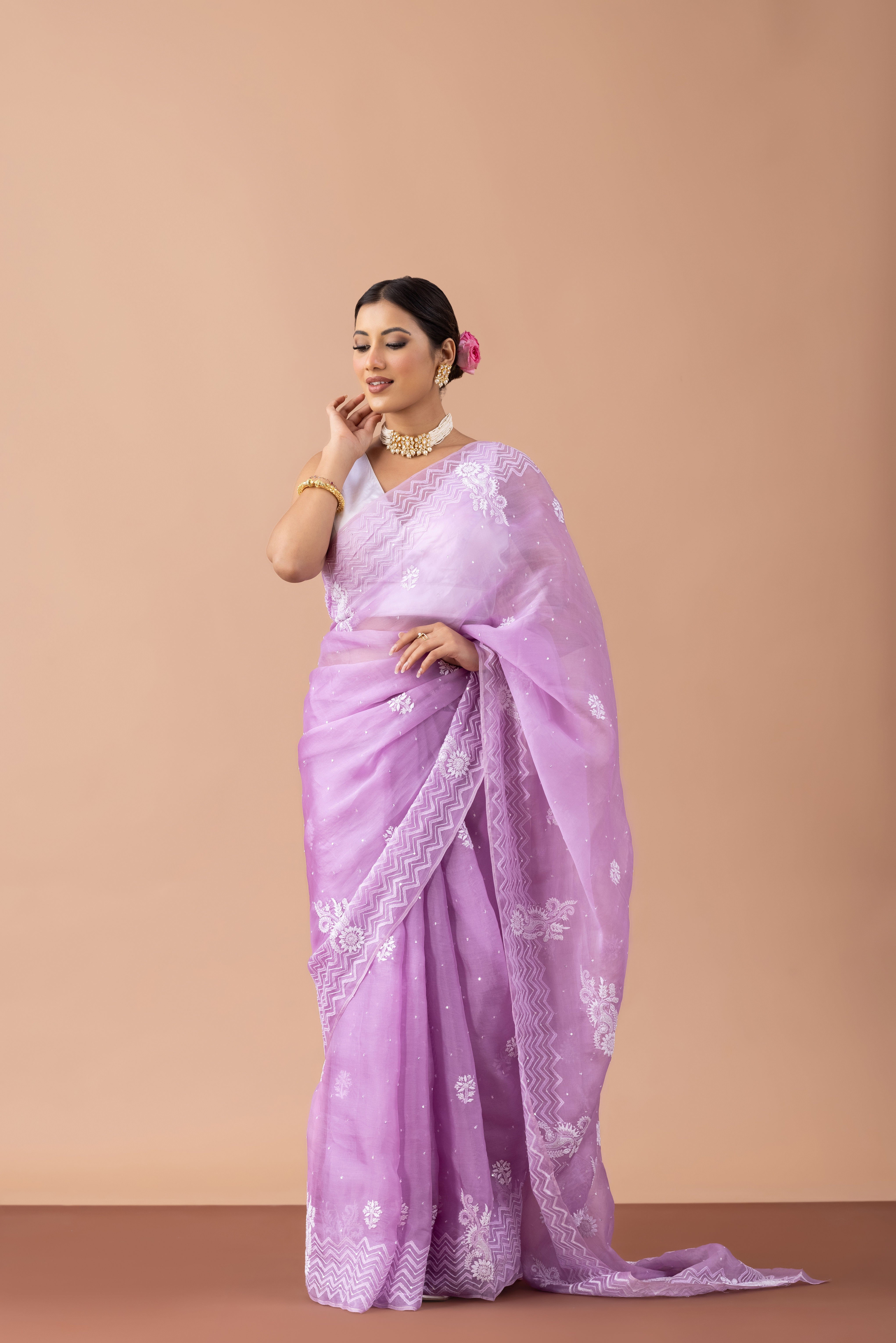 Woman wearing a lavender saree with white lace details against a beige background