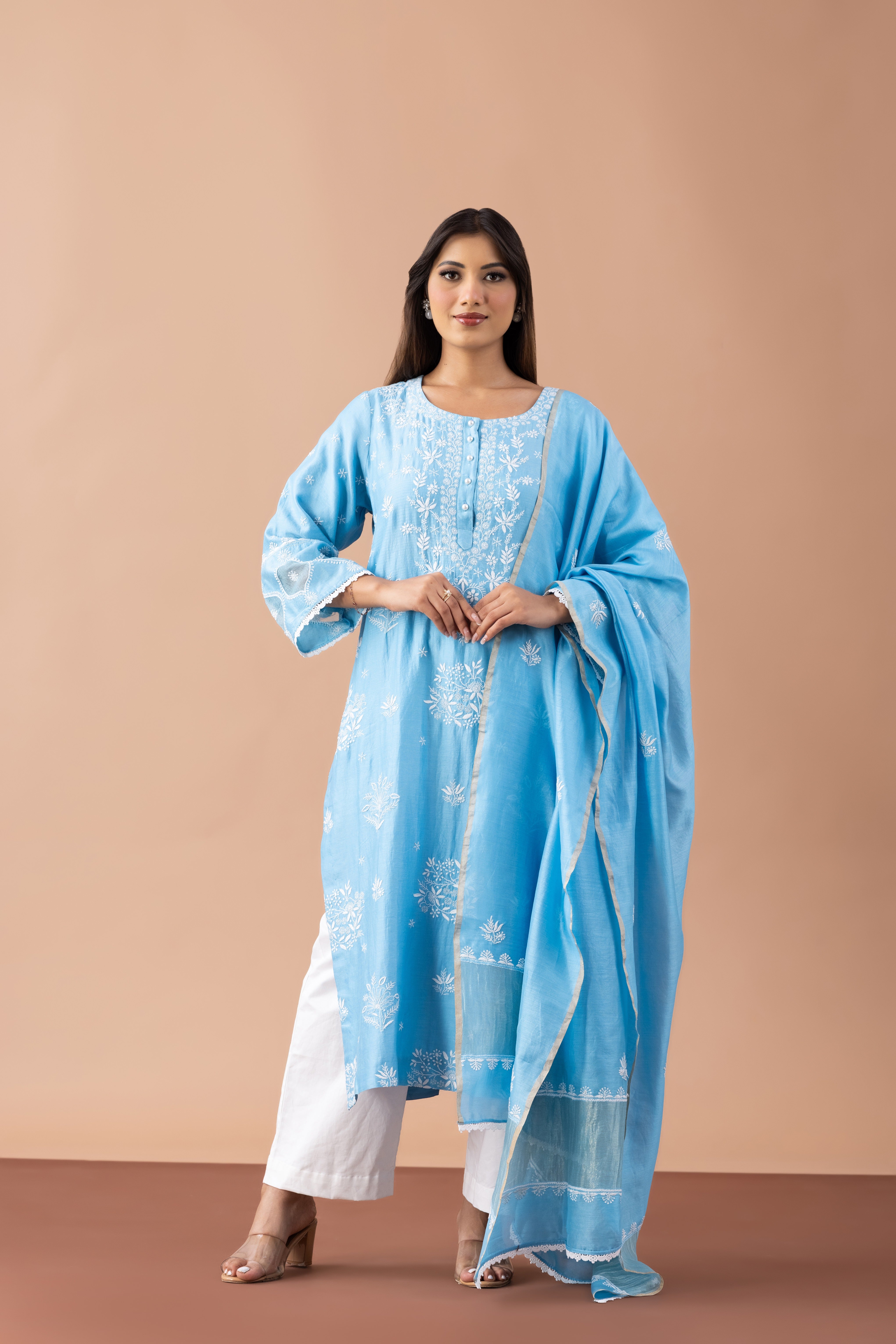 Woman wearing a light blue traditional outfit with white pants against a beige background