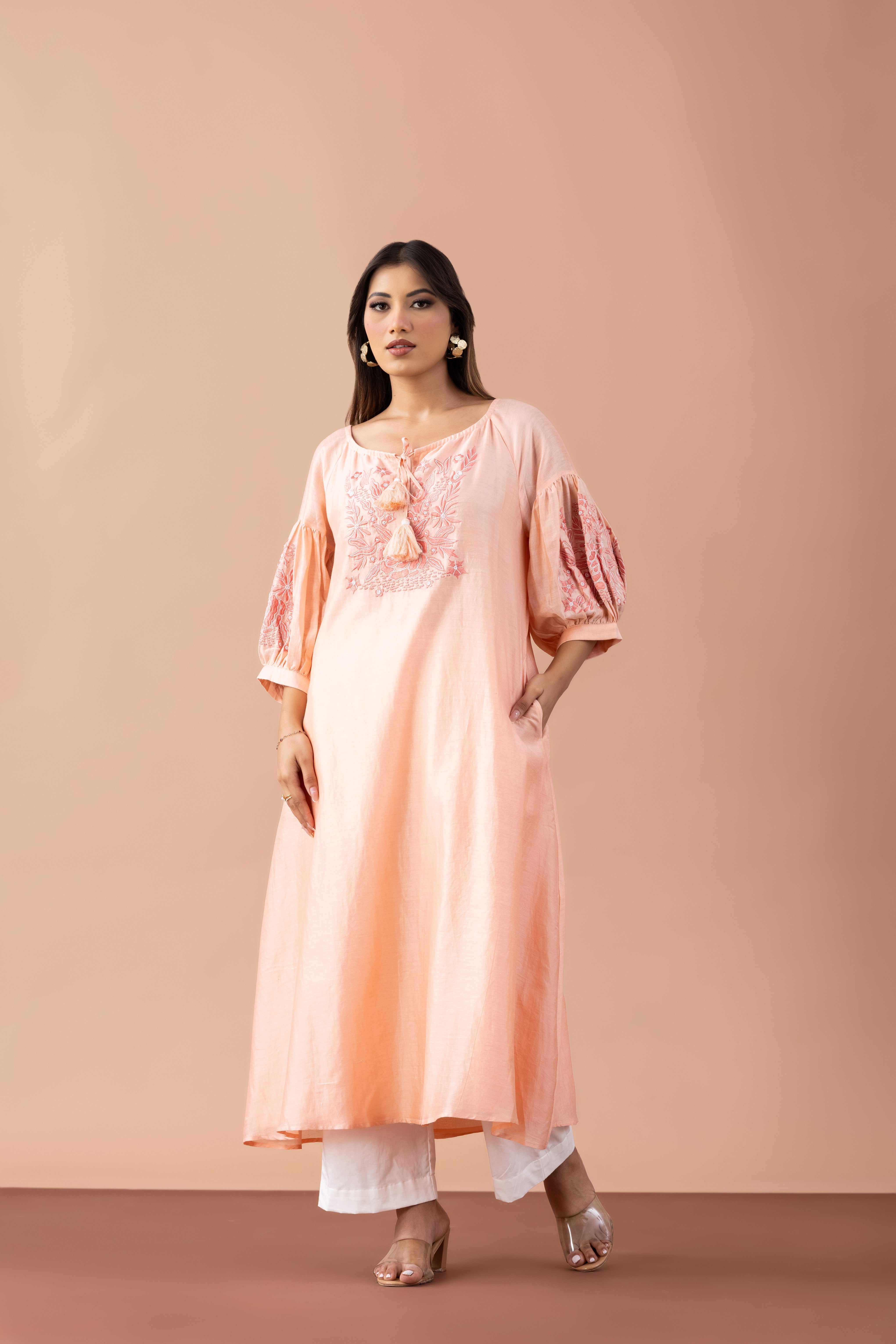 Woman wearing a peach-colored dress with floral details on a beige background