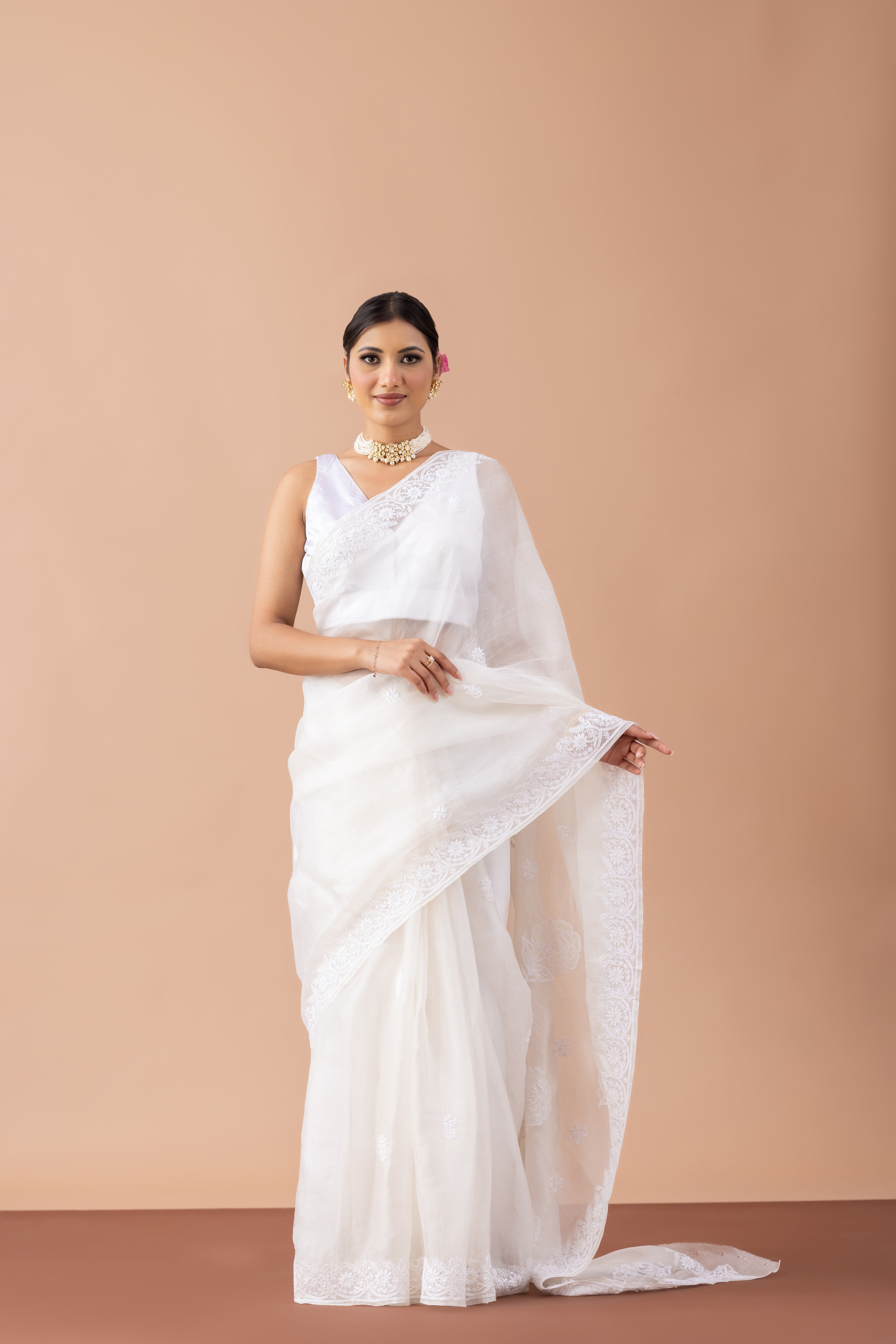 Woman wearing a white saree against a beige background